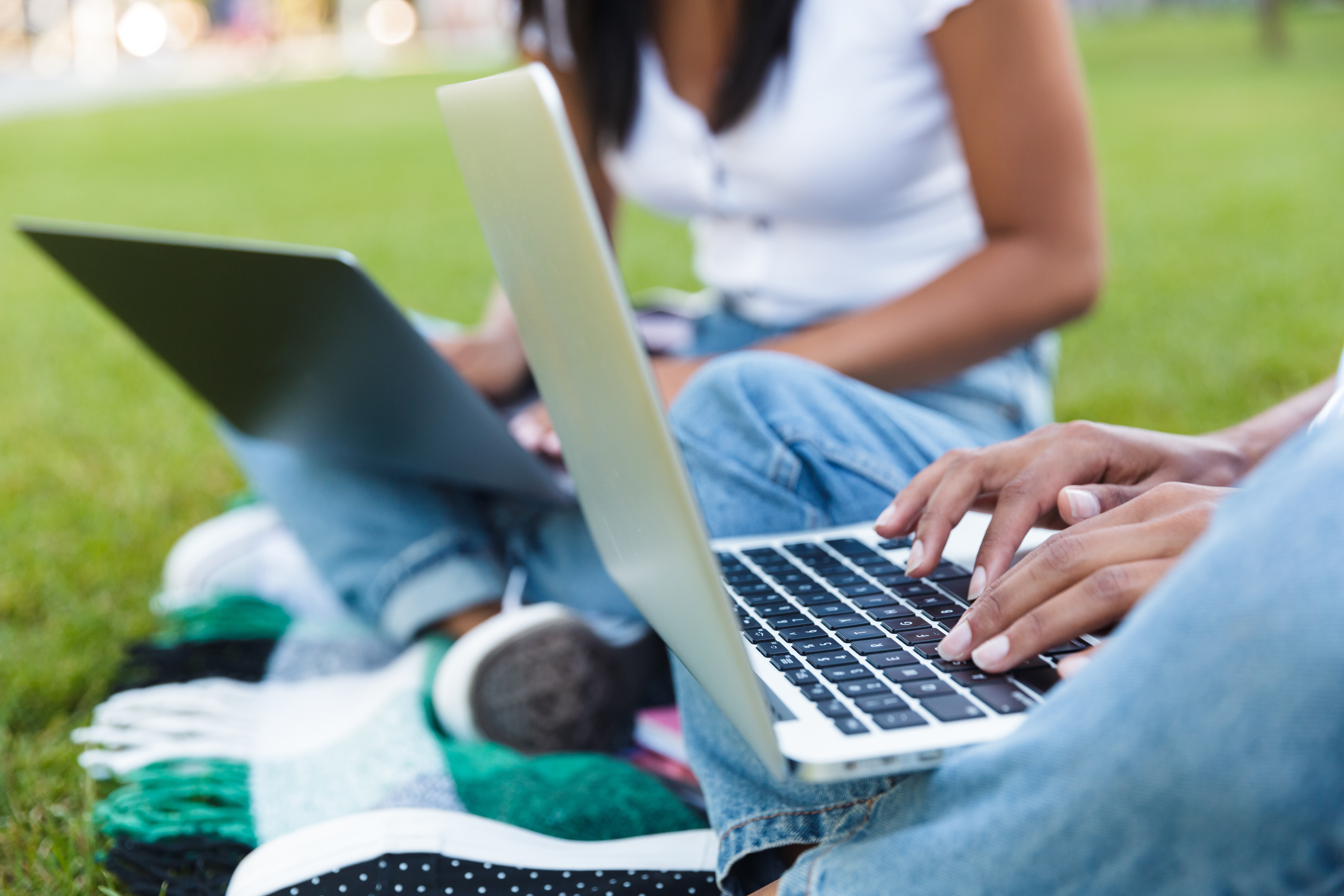 Two people sitting on the grass working on their laptops.