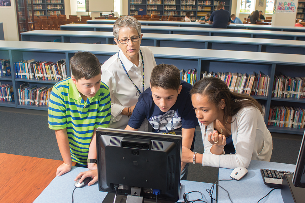 Students doing computer work while the teacher looks on Students doing computer work while the teacher looks on