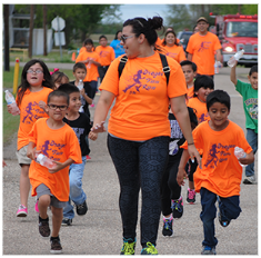Adults leading students and others as they walk down the street in a parade