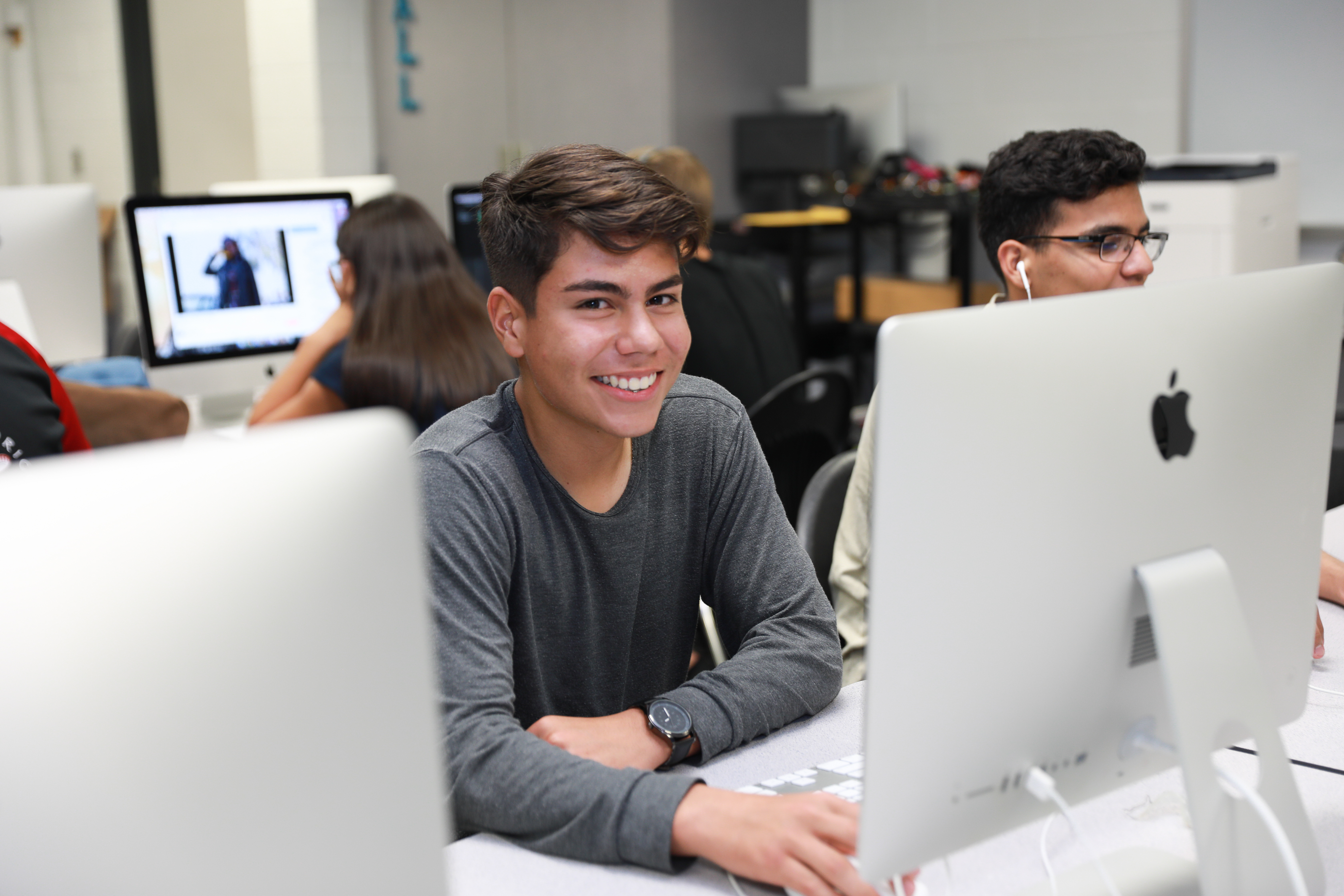 Teenager smiling at the camera with other students working in a computer lab