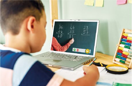 Boy working on an assignment and watching the lesson on his laptop.