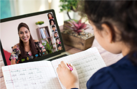 Girl writing in notebook and watching teacher on her laptop.